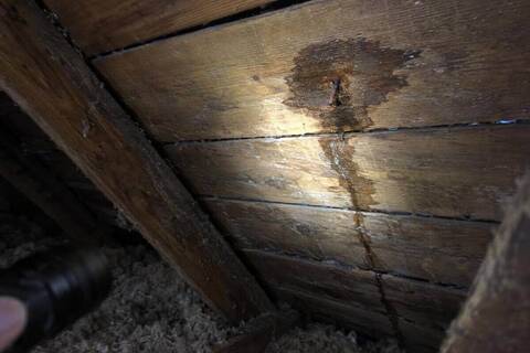 Flashlight beam on the underside of roof decking in an attic with a dark stain around a nail