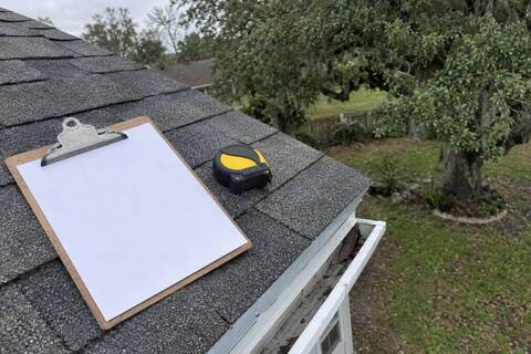 Blank clipboard and tape measure resting on a roof edge above a drip edge and gutter