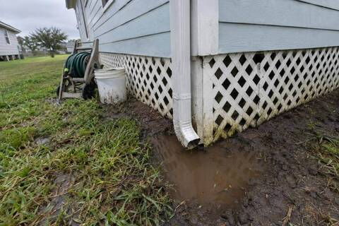 Downspout ending beside the skirting of a pier-and-beam house with standing water on the soil