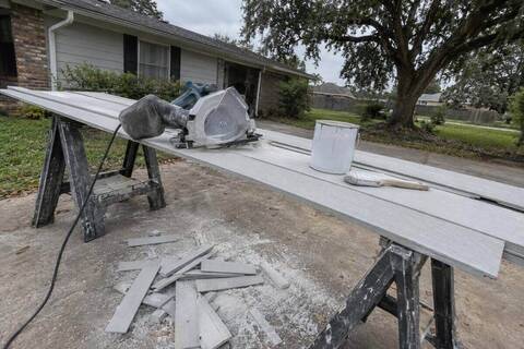 Fiber-cement planks on sawhorses with a dust shroud saw and a stack of cut offcuts