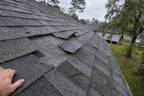 Composition shingles lifted and creased along a roof slope with a tab missing and felt showing