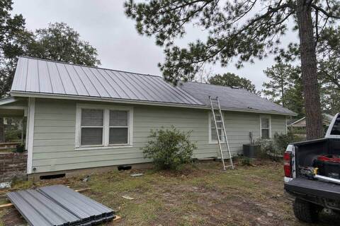 Standing seam metal panels partly laid on a single-story house with lap siding