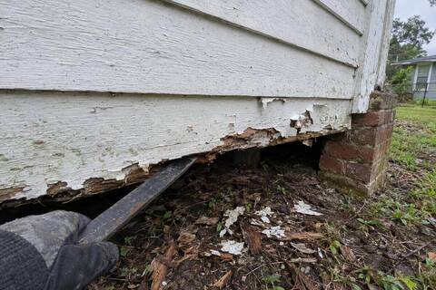 Rotted bottom courses of painted wood lap siding with a pry bar behind one board
